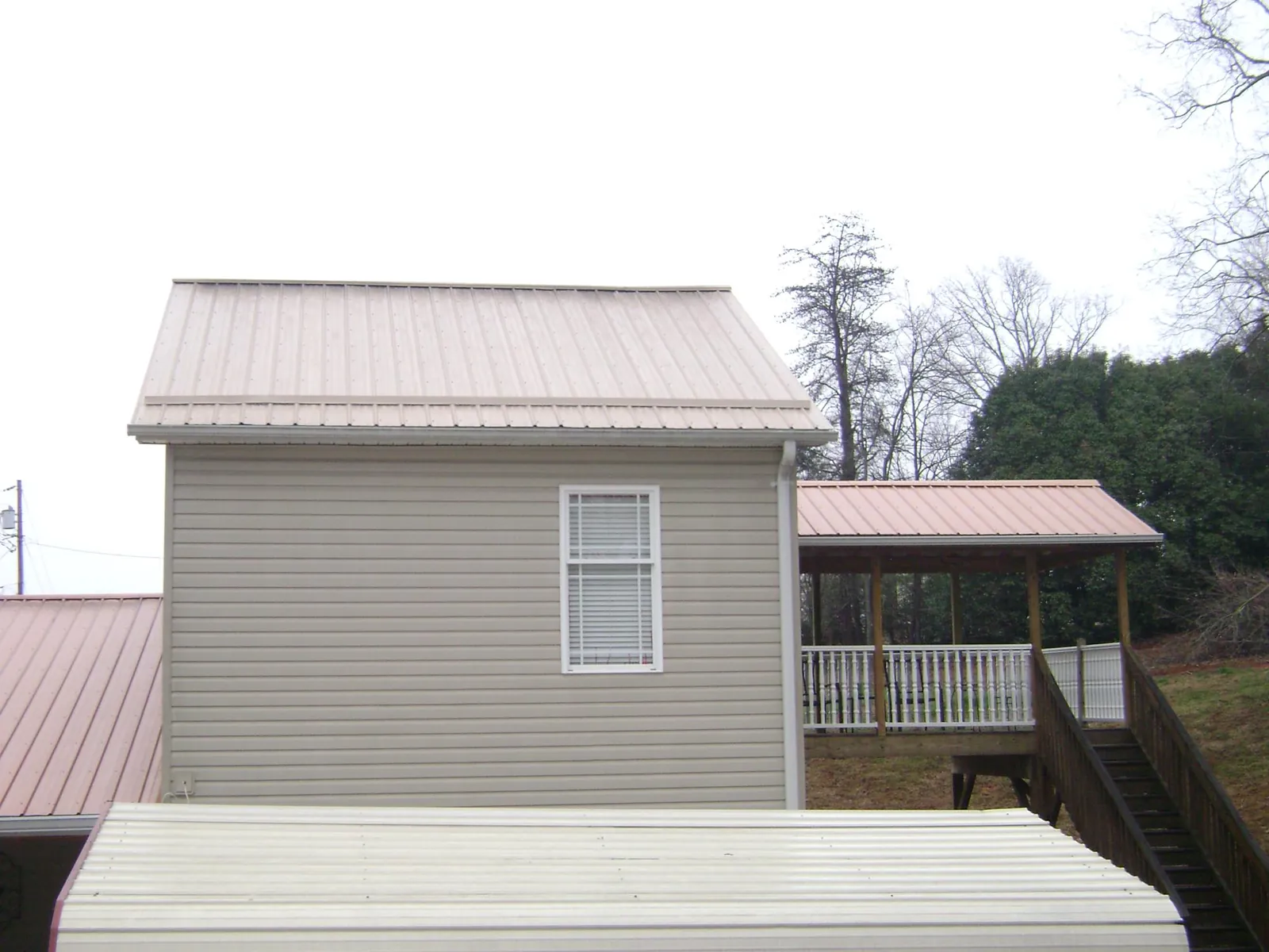Tan metal roofs on a two story addition and attached porch, from a Roof Replacement job in Jefferson